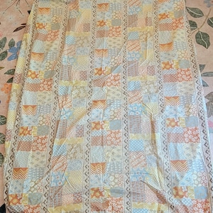 May include: A patchwork quilt with a mix of geometric and floral patterns in beige, orange, blue, and yellow. The quilt has vertical patterned borders and a mix of square and rectangular patches, creating a vintage aesthetic.