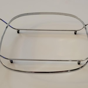 Peut inclure: Un support de plat de service en métal chromé doté d'un cadre rectangulaire aux coins arrondis, de quatre petits pieds et de deux longues poignées cylindriques en bois brun foncé fixées par des supports métalliques incurvés.