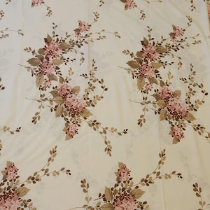 Può includere: Un tessuto color crema caratterizzato da un motivo floreale ripetuto. Il design è composto da grappoli di piccoli fiori rosa e marrone scuro con foglie marroni e steli sottili e rampicanti disposti in modo simmetrico e spaziato sulla superficie.