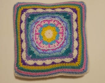 May include: A square crochet pillow featuring a circular mandala-style center in yellow, light blue, and pink. The design transitions into a square shape with concentric borders of white, teal, purple, yellow, and pink yarn in various stitches.