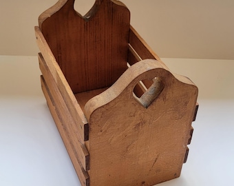 May include: A rectangular wooden crate with a medium brown finish, featuring slatted sides and two tall end panels. Each end panel has a cutout heart shape at the top center, serving as a handle for carrying the open-topped storage container.