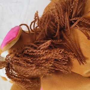 Puede incluir: Cabeza de caballo de peluche marr&oacute;n con una oreja rosa. El caballo tiene una melena rizada marr&oacute;n y un hocico blanco. El juguete est&aacute; hecho de material suave, probablemente dise&ntilde;ado para ni&ntilde;os.
