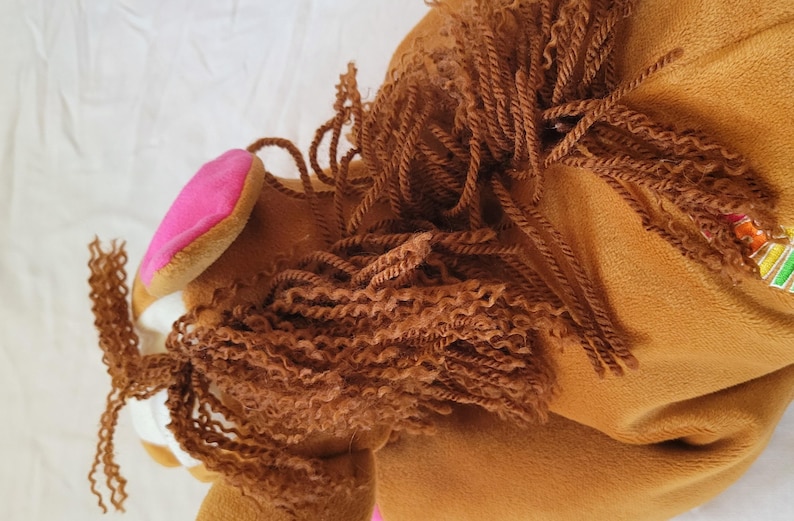 Puede incluir: Cabeza de caballo de peluche marr&oacute;n con una oreja rosa. El caballo tiene una melena rizada marr&oacute;n y un hocico blanco. El juguete est&aacute; hecho de material suave, probablemente dise&ntilde;ado para ni&ntilde;os.