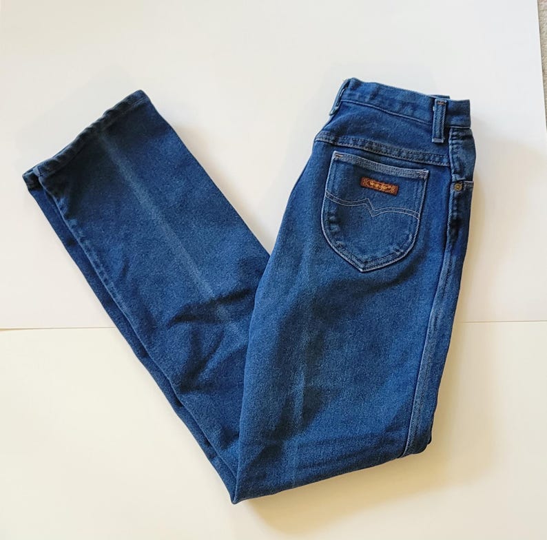May include: Dark blue denim jeans with a straight leg design. The jeans have a high waist and a back pocket with a brown label. The jeans are made of a durable denim material.