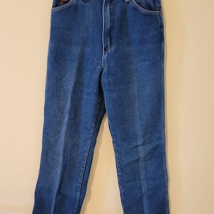 May include: A pair of blue denim jeans hanging on a white hanger. The jeans feature a classic five-pocket design, a button and zip fastening, and a straight leg cut. The denim is a medium wash with subtle fading.