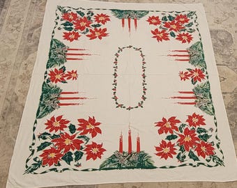 May include: A rectangular off-white tablecloth featuring a festive holiday print. The design includes clusters of red poinsettia flowers with green leaves, sets of three red taper candles with pine boughs, and a central oval holly berry wreath.