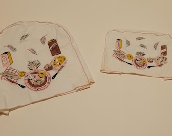 May include: Two off-white fabric covers with pink trim, featuring a printed pattern of food items including bread, plates, and containers. The larger cover is rounded, while the smaller cover is rectangular, both displaying a culinary theme.