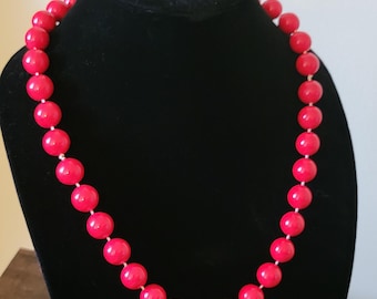 May include: A red beaded necklace on a black velvet display stand. The necklace is made of large, round beads.