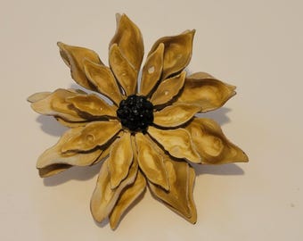 May include: A flower-shaped brooch featuring layered, pointed petals in shades of tan and cream with a marbled finish. The center of the flower is a cluster of small, dark black beads that provide a high-contrast focal point to the light petals.