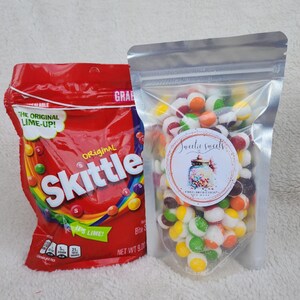 May include: A red bag of Skittles Original Lime candy with a clear plastic bag of colorful candy-coated chocolate balls. The bag of chocolate balls has a sticker that says "Sweettie Sweets" and "Freeze Dried Candy"