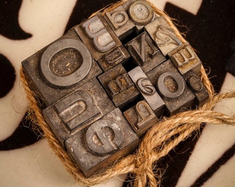 May include: A collection of vintage metal letterpress printing blocks, tied together with twine, spelling out the word "ONE".