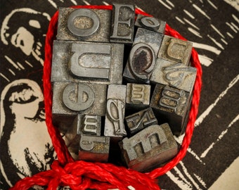 May include: A collection of vintage metal letterpress printing blocks tied together with a red cord. The blocks spell out the word "QUEUE".