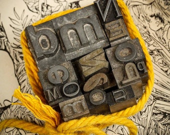 May include: A collection of metal letterpress printing blocks tied together with a yellow rope. The blocks spell out the word "mom".