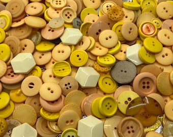 May include: A large collection of yellow and orange buttons of various sizes and shapes. The buttons are made of plastic and have a smooth, shiny finish.