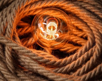 May include: A glowing light bulb sits in a nest of brown braided rope.