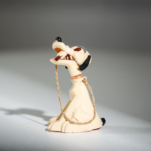 Könnte beinhalten: Cremefarbene Hunde-Figur mit schwarz-weißem Kopf, offenem Maul und brauner Seilleine. Der Hund sitzt mit offenem Maul und rotem Halsband. Die Figur hat schwarze Akzente an den Füßen.