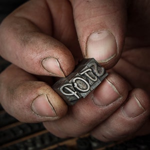 May include: Close-up of a hand holding a metal printing block with the word "STOP" embossed on it.