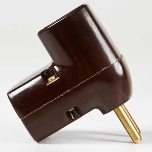 Può includere: Una spina elettrica in plastica marrone con due puntine dorate. La spina è angolata e ha una forma arrotondata.