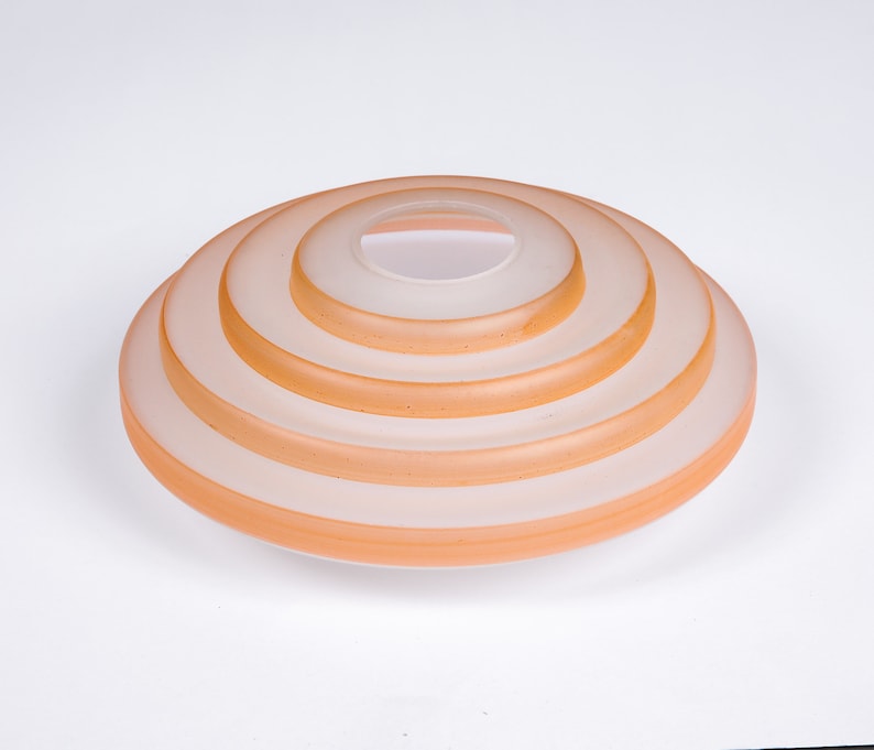 May include: A set of five concentric glass rings, each with a slightly different shade of peach, creating a layered effect. The rings are stacked on top of each other, forming a circular shape.