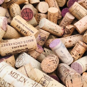 May include: A close-up image of a pile of used wine corks. The corks are made of natural cork and have a variety of colors, shapes, and sizes. Some of the corks have writing on them, including the year the wine was bottled, the name of the winery, and the region where the grapes were grown.
