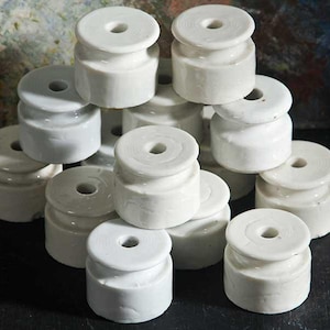 Peut inclure: Une collection d'isolateurs en céramique blanche. Chaque isolateur a un corps cylindrique avec un dessus circulaire et un trou au centre. Les isolateurs sont empilés, mettant en valeur leur design et leur forme.