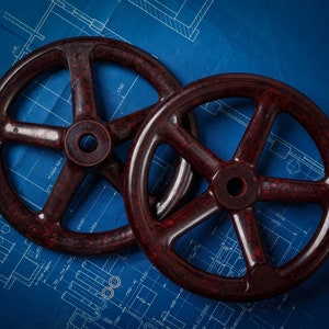 Pode incluir: Dois grandes carretéis de madeira de cor vermelha escura com seis raios cada um, sobre um fundo azul com linhas brancas.