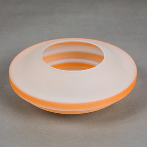 May include: A white ceramic bowl with a wide, shallow opening and a layered, orange rim. The bowl is designed to hold small items, such as flowers or decorative objects.