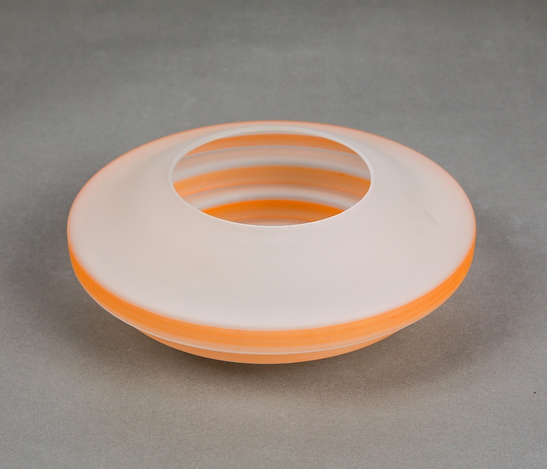 May include: A white ceramic bowl with a wide, shallow opening and a layered, orange rim. The bowl is designed to hold small items, such as flowers or decorative objects.