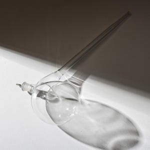 Puede incluir: Una taza de cerámica blanca con un asa negra y el texto "But First, Coffee" en negrita negra. La taza está llena de un líquido oscuro, probablemente café, y se encuentra sobre una superficie de color claro.