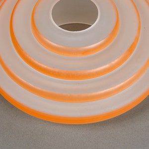 May include: A white frosted glass lampshade with a series of concentric orange rings.