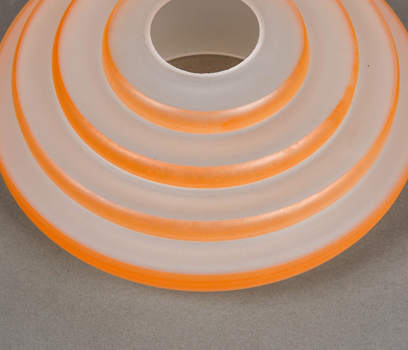 May include: A white frosted glass lampshade with a series of concentric orange rings.