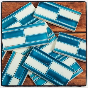May include: A collection of blue and white ceramic tiles with a geometric pattern. The tiles are arranged in a random pattern on a wooden surface.