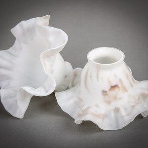 May include: Two white ruffled lampshades, one with a plain white finish and the other with a brown and white marbled finish.