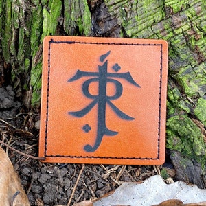 May include: A brown leather patch with a black symbol, resembling a stylized letter "F", on a tree trunk background.