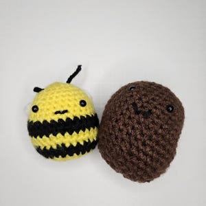 May include: Two handmade crochet amigurumi figures: a yellow bee with black stripes and a brown potato. Both have black eyes and stitched facial features. The bee has a small black antenna. The items are set against a white background.