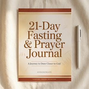 May include: A journal with the text "21-Day Fasting & Prayer Journal" in brown lettering. The journal has a cream-coloured background with a brown border. A white pen rests beside the journal. The text "A Journey to Draw Closer to God" is also visible.