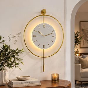 May include: A circular wall clock featuring a gold metal frame and a white face with gold hands and markers. The clock displays the numbers 12 and 6, includes a vertical gold pendulum, and emits a soft warm light from behind the clock face.