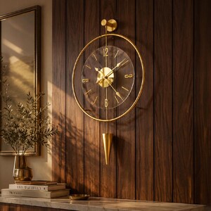 May include: A circular wall clock featuring a gold metal frame and a transparent acrylic face. The clock has gold hands, gold hour markers, and the numbers 12 and 6 in gold. A gold vertical rod extends from the top to a gold cone-shaped pendulum.
