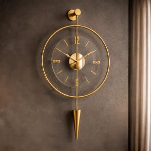 May include: A gold-toned wall clock featuring a circular frame and a transparent face. The clock has a central gold disc, thin gold hands, and gold numerals at the 12, 3, 6, and 9 positions. A vertical gold rod extends to a cone-shaped pendulum.