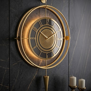 Könnte beinhalten: Eine goldfarbene Wanduhr mit römischen Ziffern und einem Pendel. Die Uhr hat ein kreisförmiges Design mit schwarzem Zifferblatt und goldfarbenem Rahmen. Die Uhr ist an einer dunklen, strukturierten Wand befestigt. Zwei weiße Kerzen in goldenen Haltern befinden sich unten rechts.