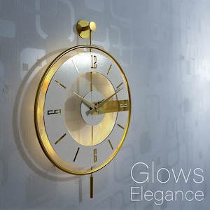 Peut inclure: Une horloge murale ronde dorée avec un cadran blanc et des chiffres noirs. L'horloge a un design minimaliste avec un cadre et des aiguilles dorées. Le texte "Glows Elegance" est visible en bas à droite.
