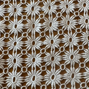 Può includere: Tessuto di pizzo all'uncinetto bianco con un motivo ripetitivo di fiori e cerchi.