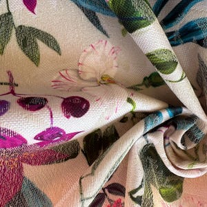 May include: A close-up of a white fabric with a floral print. The fabric features pink, purple, and green flowers, as well as blue and green leaves.