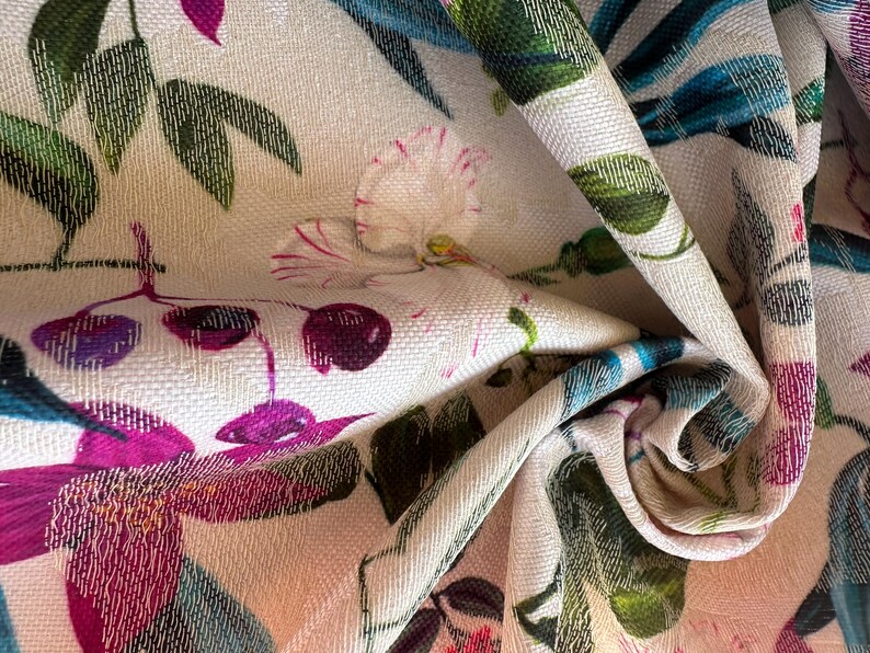 May include: A close-up of a white fabric with a floral print. The fabric features pink, purple, and green flowers, as well as blue and green leaves.