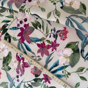 May include: A beige fabric with a floral print featuring pink, white, and green flowers. The fabric has a textured surface and a repeating pattern.