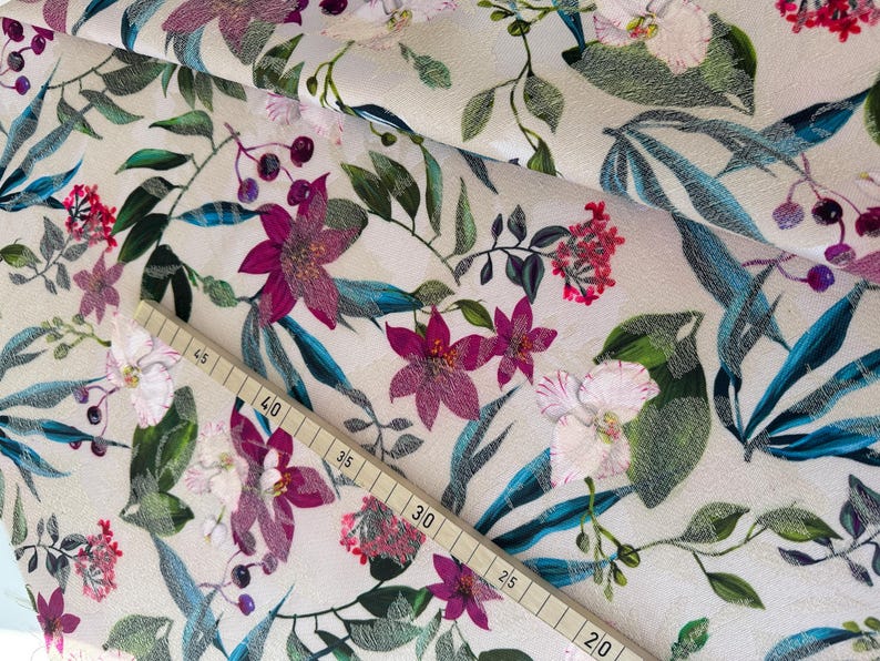 May include: A beige fabric with a floral print featuring pink, white, and green flowers. The fabric has a textured surface and a repeating pattern.