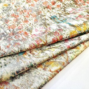 May include: A close-up of a fabric with a colorful, abstract pattern. The fabric is folded in layers, revealing a silver metallic sheen.