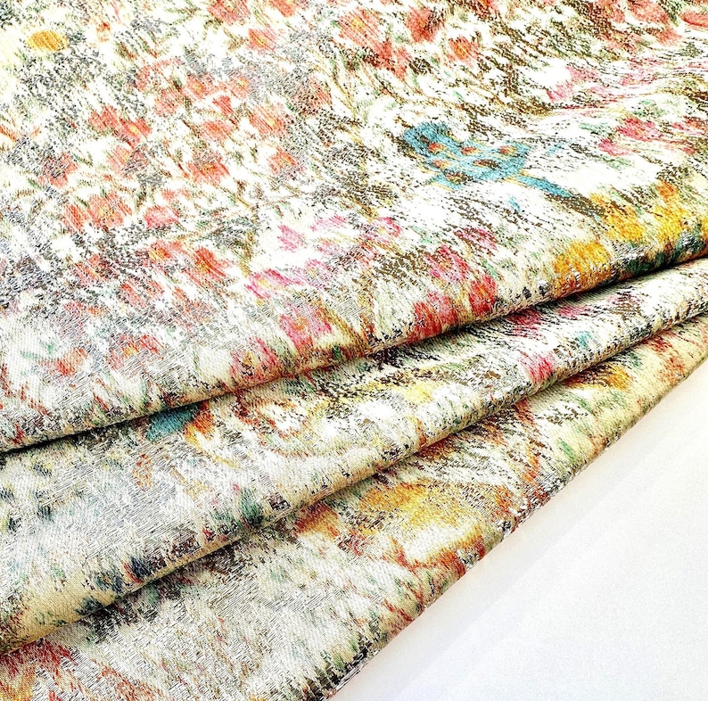 May include: A close-up of a fabric with a colorful, abstract pattern. The fabric is folded in layers, revealing a silver metallic sheen.