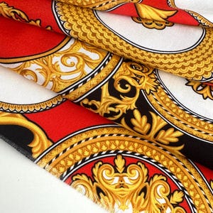 Könnte beinhalten: Roter Stoff mit einem goldenen und schwarzen Barockmuster. Der Stoff zeigt ein sich wiederholendes Muster aus verzierten Kreisen mit komplizierten Details.