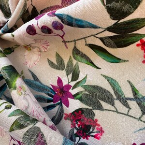 May include: A close-up of a white fabric with a floral print. The fabric features pink, purple, and green flowers on a white background.